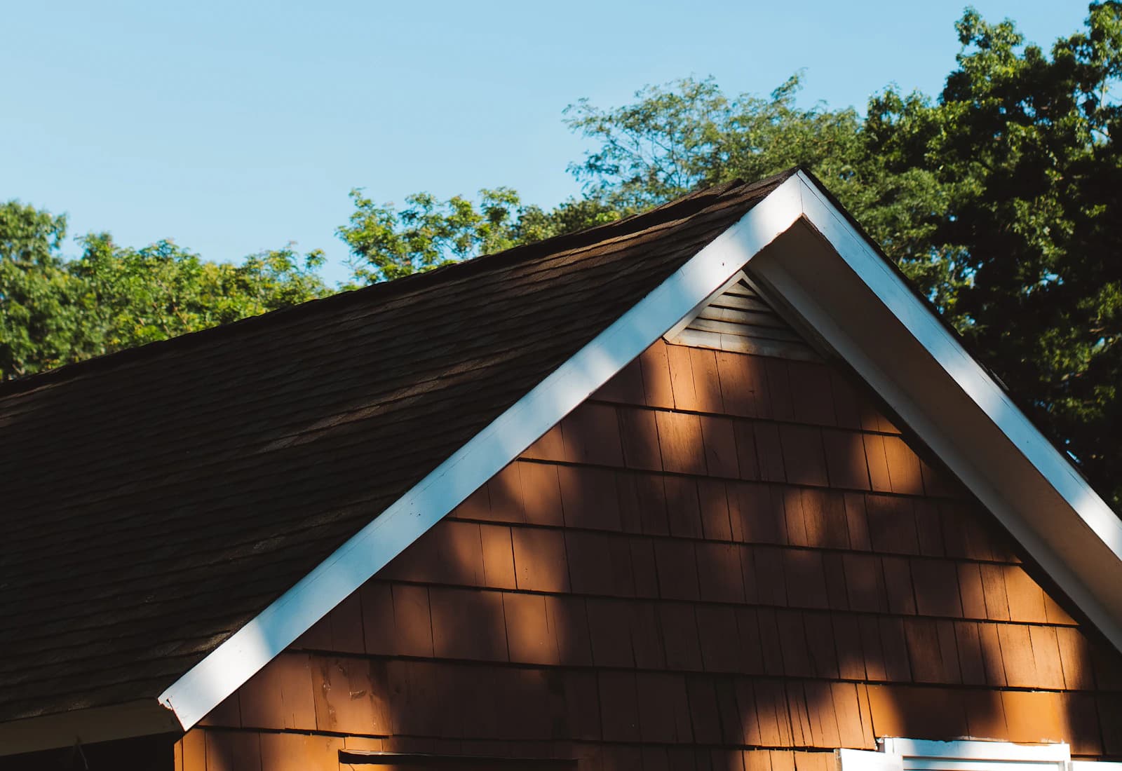Wood-shingled gable and white roof trim beneath a blue sky