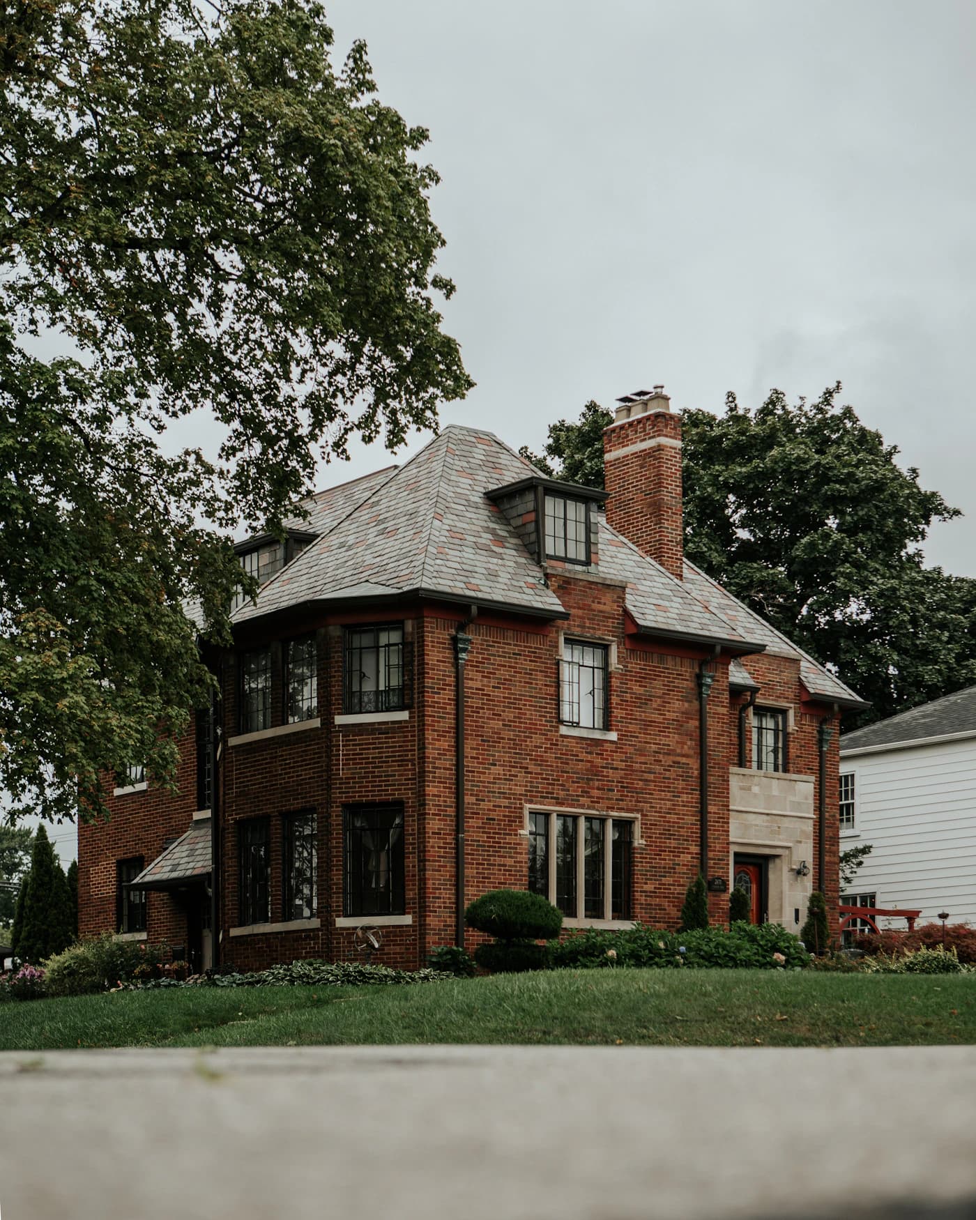 Mature tree beside a brick home with a steep roof